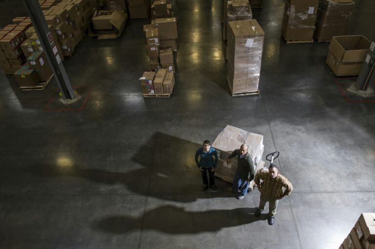 A group of three warehouse workers standing in the center of a distirbution warehouse.